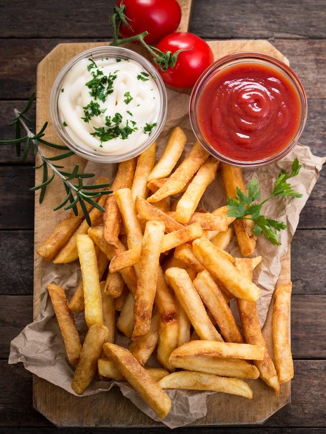 Porção de batata frita crocante servida com maionese e ketchup